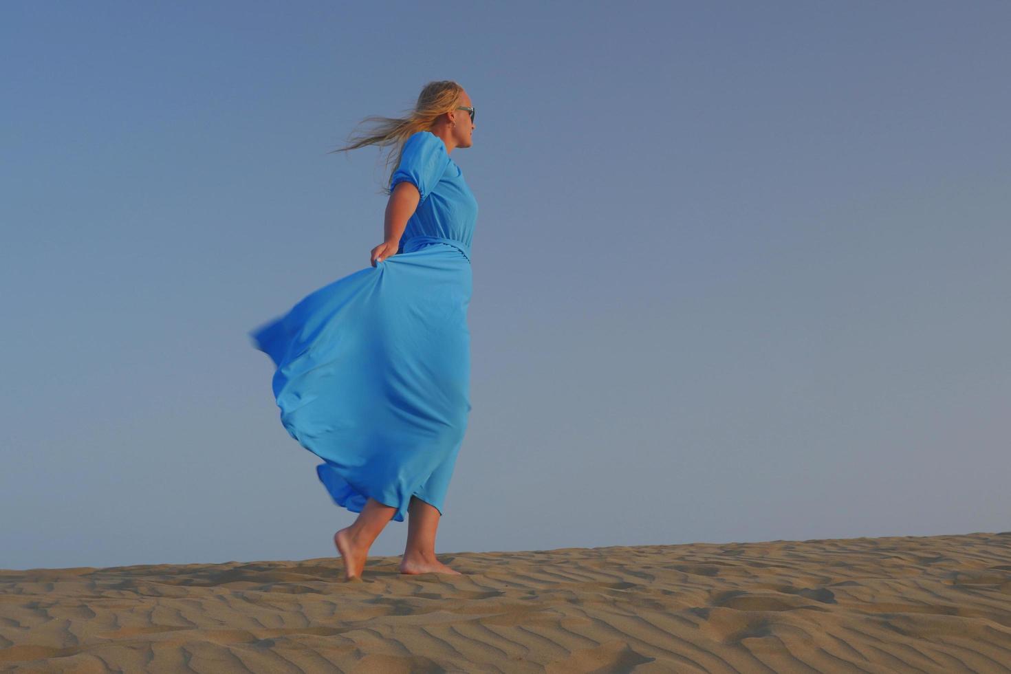 Barfußfrau, die im Sand in einem blauen Kleid geht foto