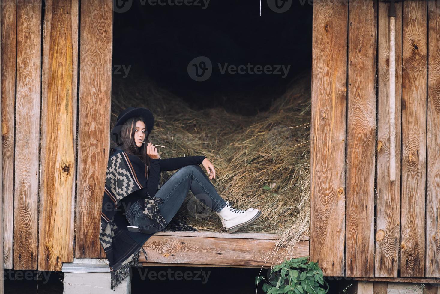 junge brünette frau, die in der scheune sitzt. Landhausstil. foto