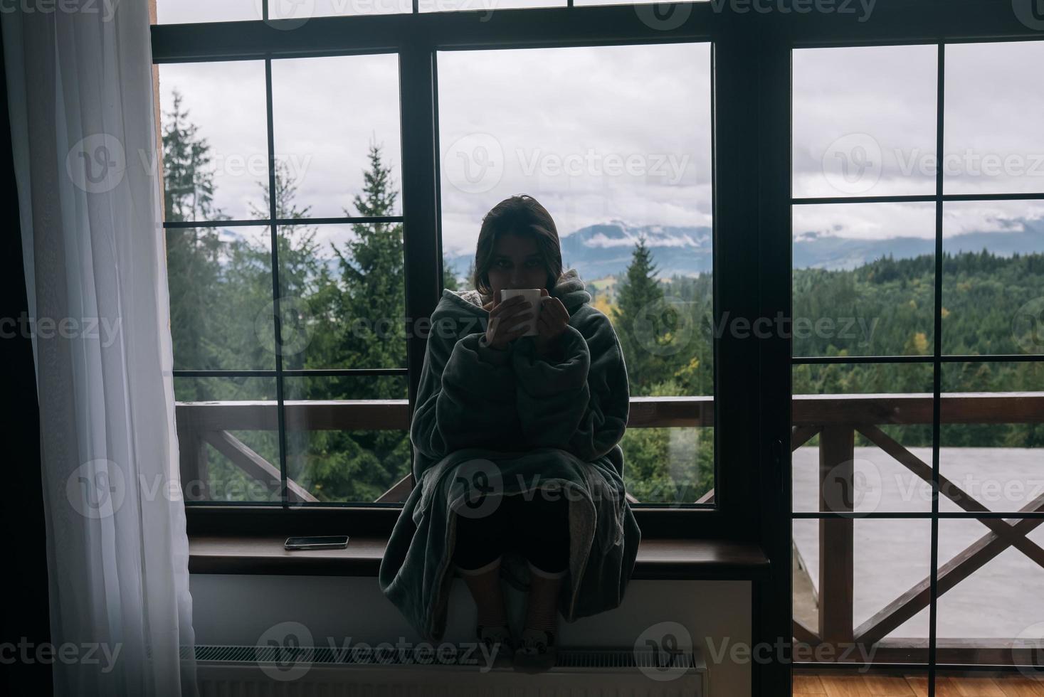 Silhouette einer Frau, die mit einem Becher auf der Fensterbank sitzt foto