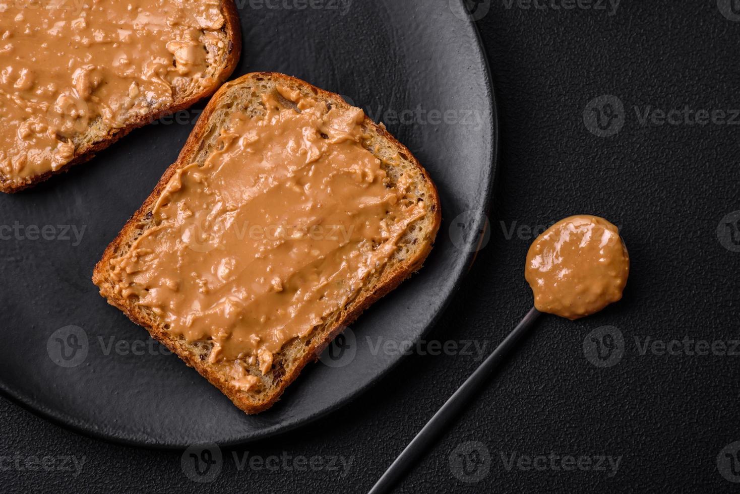 nahrhaft Sandwich bestehend aus von Brot und Erdnuss Butter auf ein schwarz Keramik Teller foto