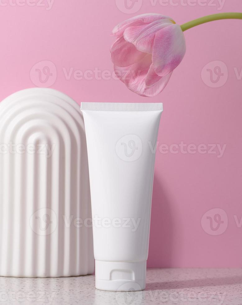 Weiß Plastik Tube zum kosmetisch Produkte auf ein Rosa Hintergrund mit ein Bogen und ein Rosa Tulpe, Werbung und branding von Produkte foto