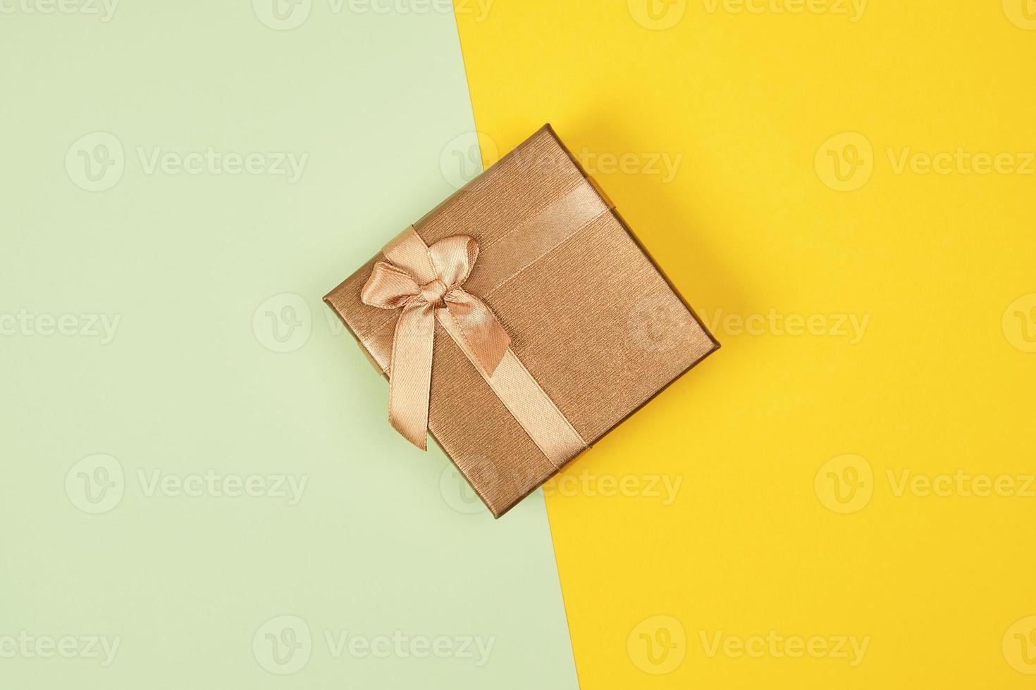 geschlossen golden Geschenk Box mit ein Bogen auf ein Grün Gelb Hintergrund foto