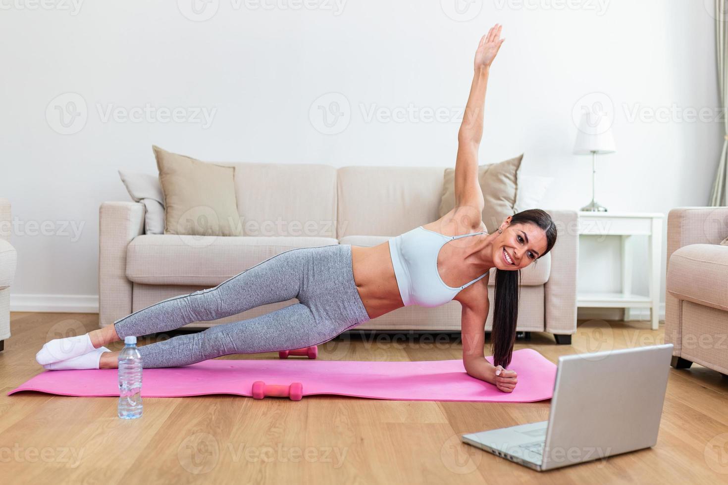 Porträt von jung attraktiv Frau tun Übungen während Aufpassen online Lektionen auf ihr Laptop. gesund Lebensstil und Sport Konzept. Schuss von Fitness Frau Sitzung auf Übung Matte foto