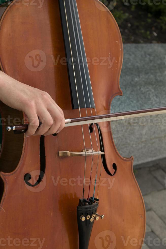 Detail von ein Mann spielen das hölzern Cello Reiben das Saiten mit das Bogen zu erhalten das Anmerkungen von ein klassisch Musik- Stück. foto