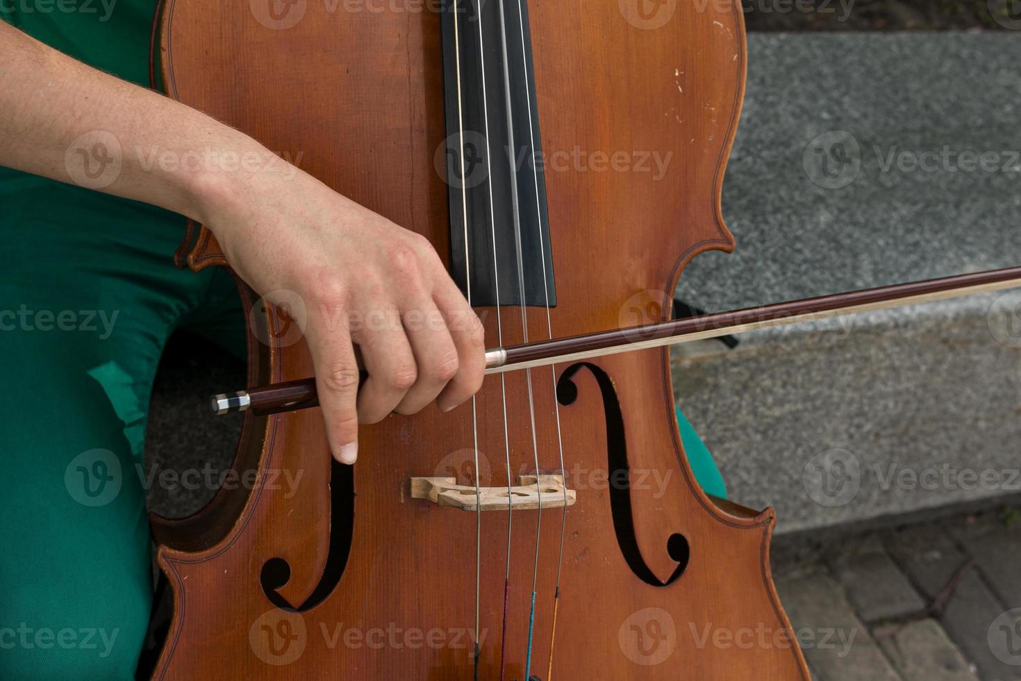 Detail von ein Mann spielen das hölzern Cello Reiben das Saiten mit das Bogen zu erhalten das Anmerkungen von ein klassisch Musik- Stück. foto