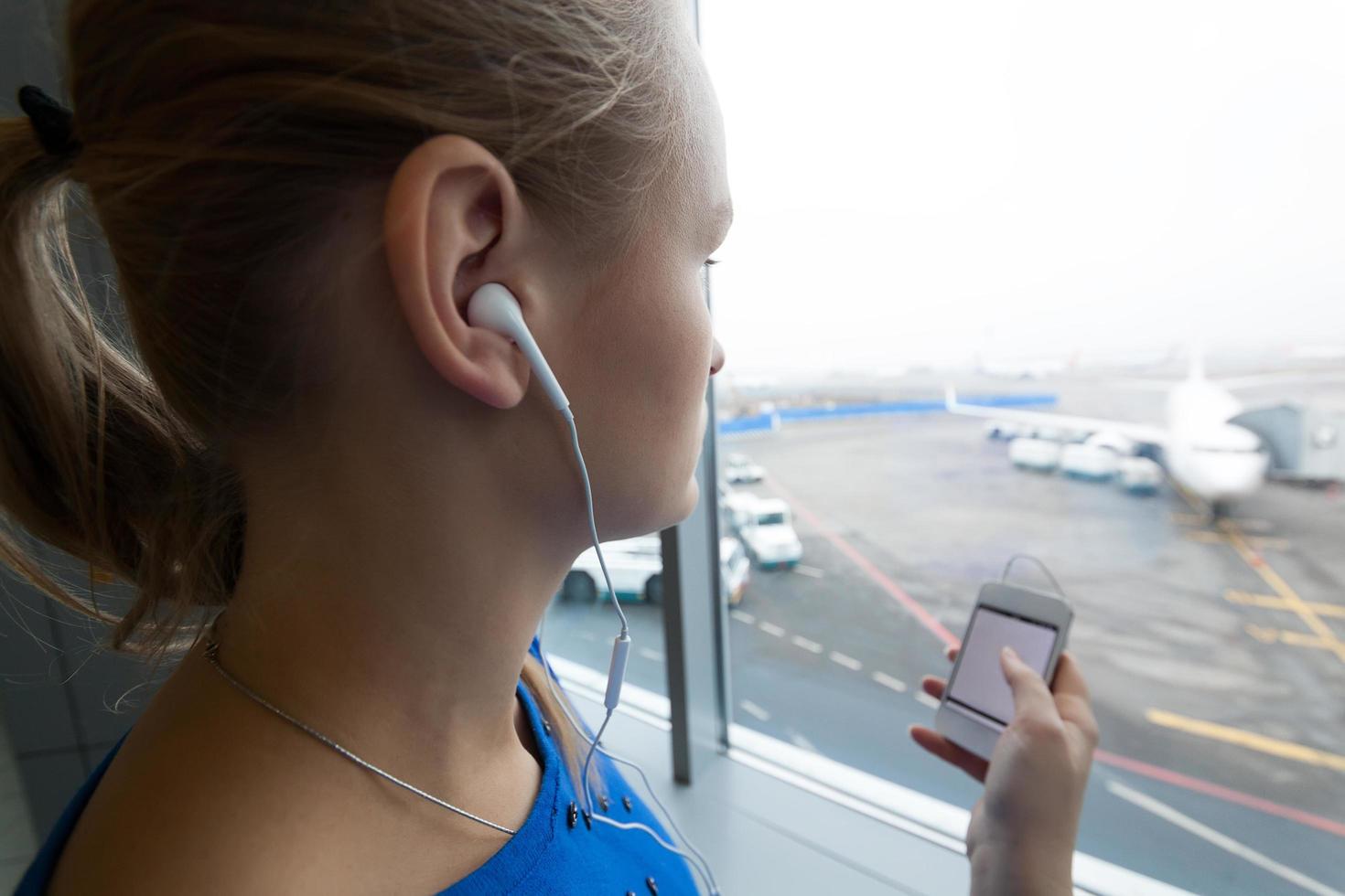 Frau, die Musik am Fenster am Flughafen hört foto