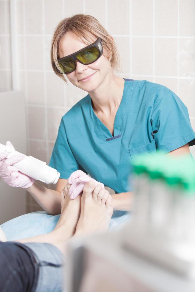 lächelnder Kosmetiker, der mit Laser arbeitet, um Füße zu behandeln foto