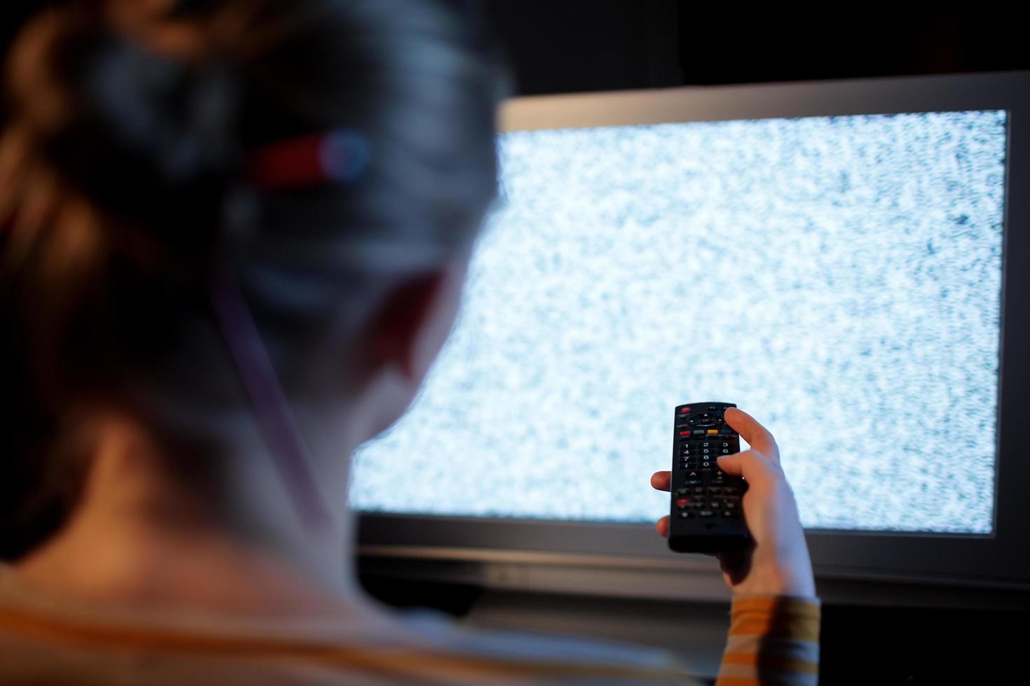 Frau mit einer Fernbedienung vor einem Fernseher foto