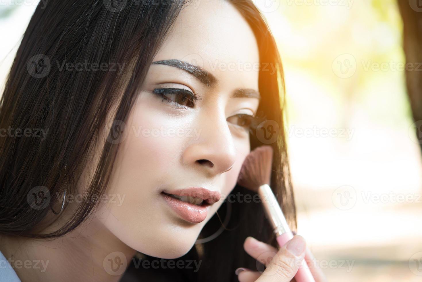 junge Frau, die Make-up Pinsel auf ihre Wange setzt foto