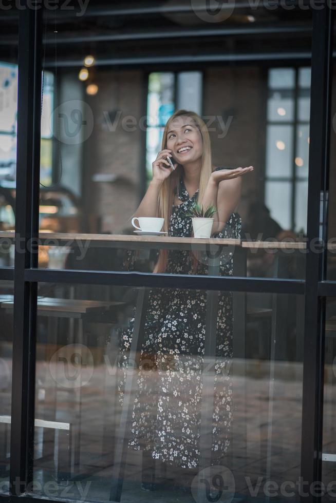 junge Frauen, die Smartphone am Fenstercafé benutzen und betrachten foto