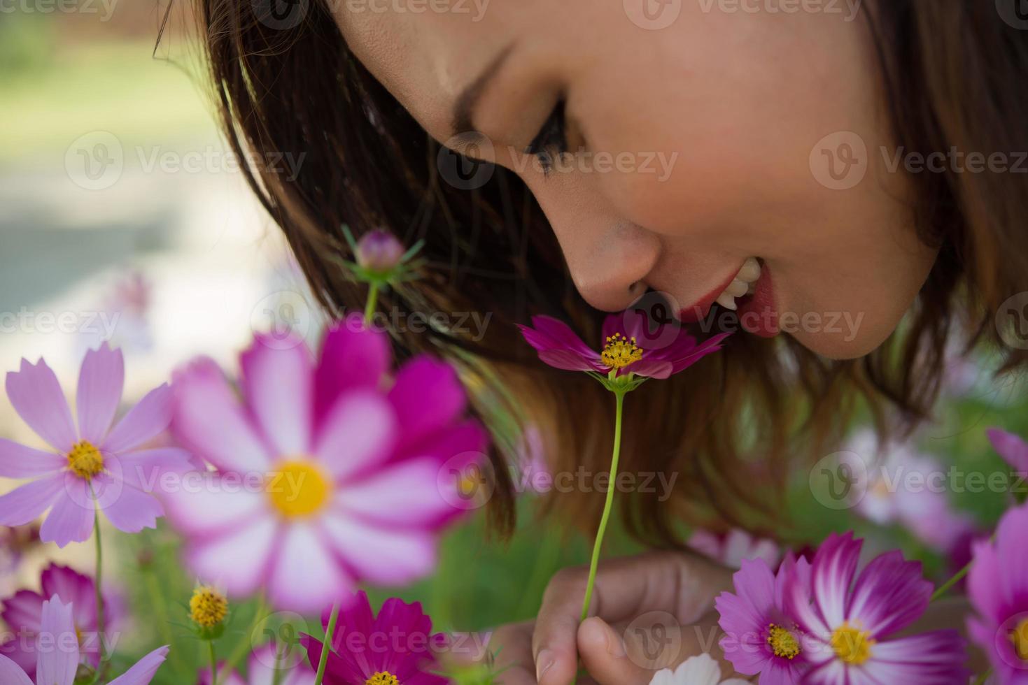 Nahaufnahme der fröhlichen Frau, die Kosmosblumen in einem Garten riecht foto