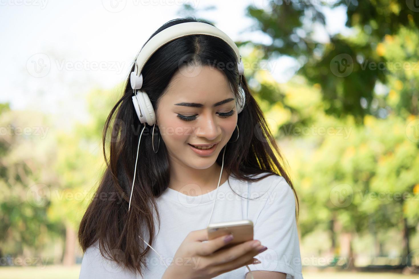 Porträt eines lächelnden Mädchens mit Kopfhörern, die Musik in der Natur hören foto