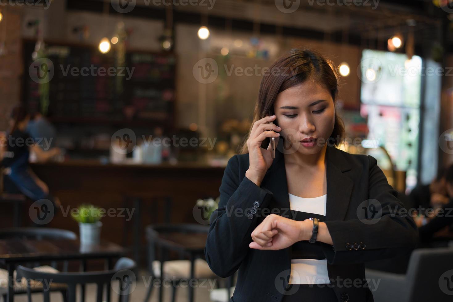 schöne Geschäftsfrau, die auf dem Handy spricht, das Handwache über Caféhintergrund betrachtet foto