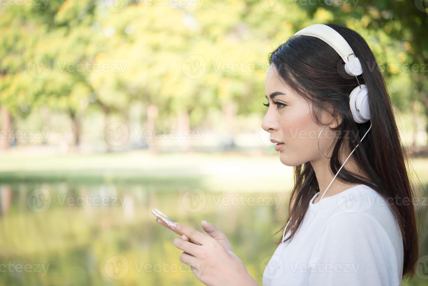 Porträt eines lächelnden Mädchens mit Kopfhörern, die Musik in der Natur hören foto