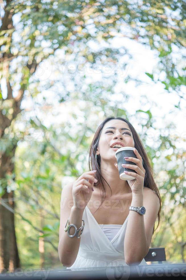 junge Frau, die wegwerfbare Kaffeetasse hält, während draußen sitzt foto
