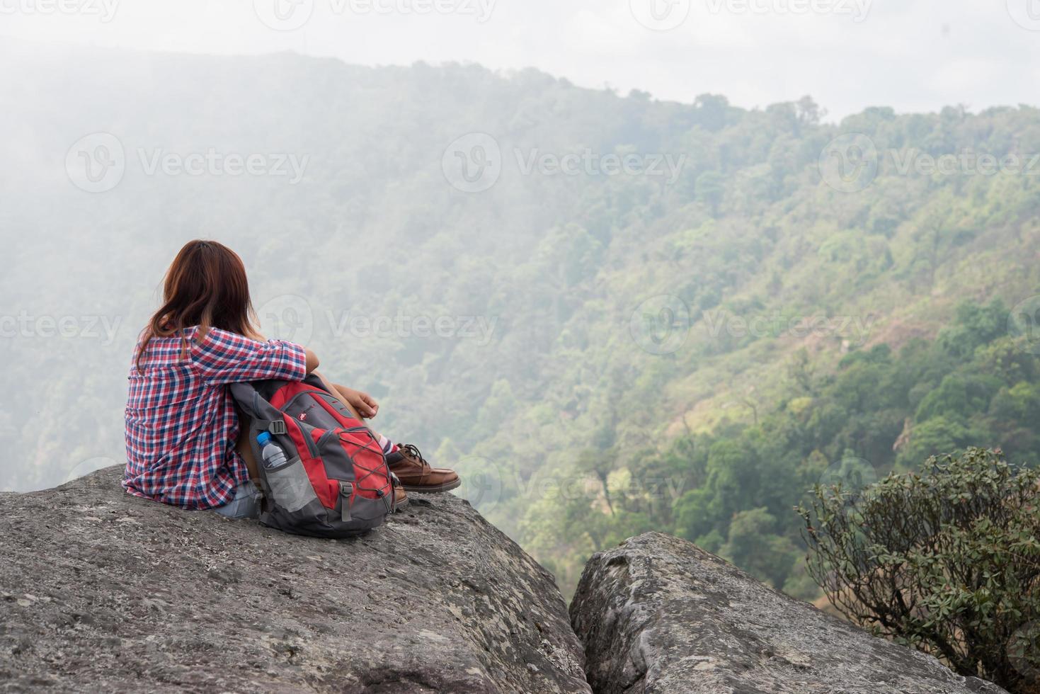 junger Wanderer mit Rucksack sitzt am Rande der Klippe foto