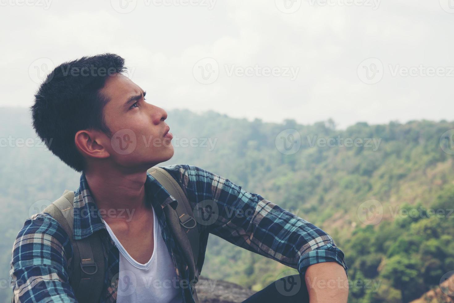 junger Hipster-Wanderer mit Rucksack, der oben auf dem Berg sitzt foto
