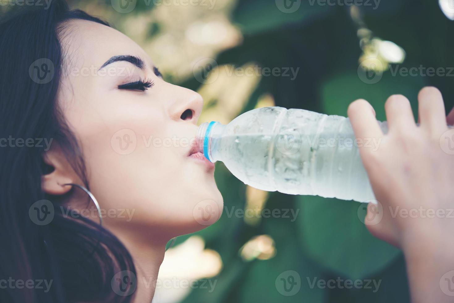 junge schöne Frau, die draußen Trinkwasser im Park entspannt foto