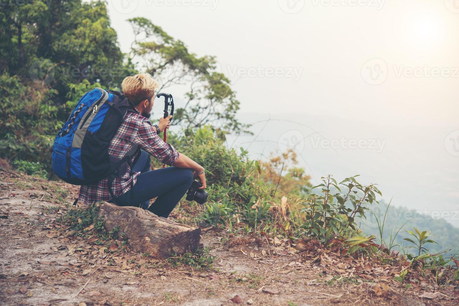 junger Hipster-Wanderer mit Rucksack, der oben auf dem Berg sitzt foto