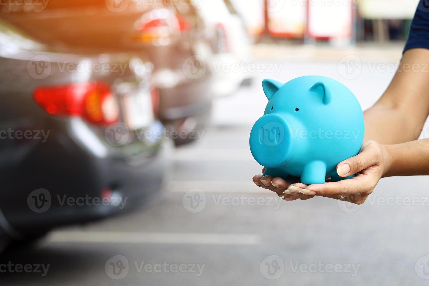 Hände halten blaues Sparschwein mit unscharfen Autos im Hintergrund foto