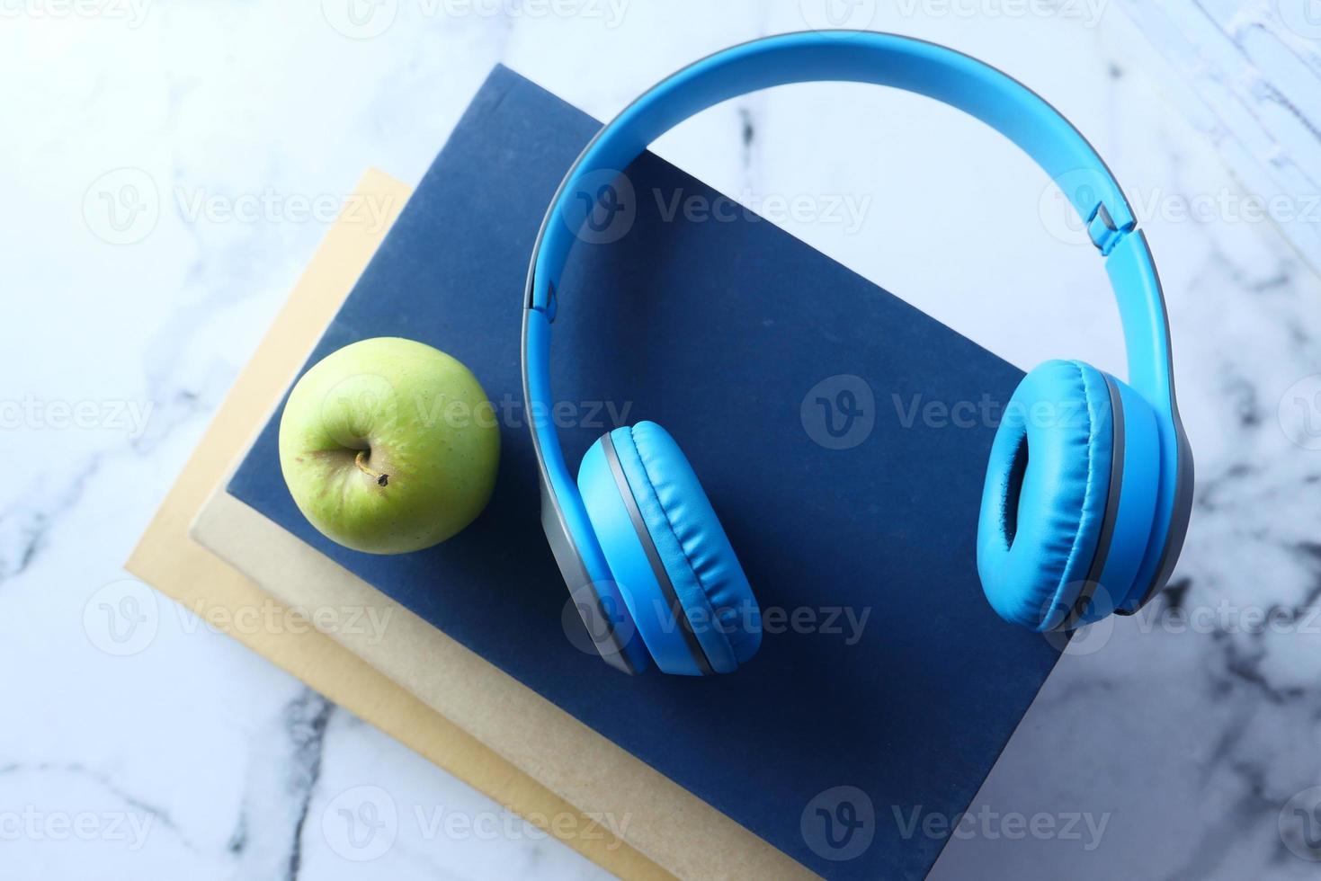 Kopfhörer und Buch mit grünem Apfel über Fliesenhintergrund foto