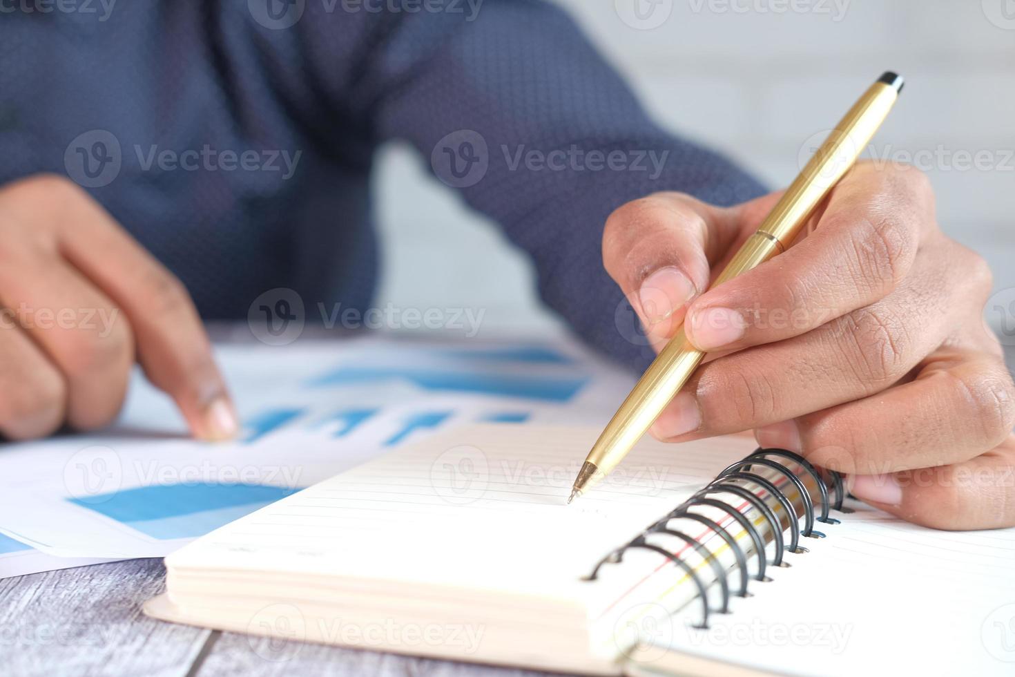 Männerhand mit Stift, der Finanzdaten analysiert und auf Notizblock schreibt foto