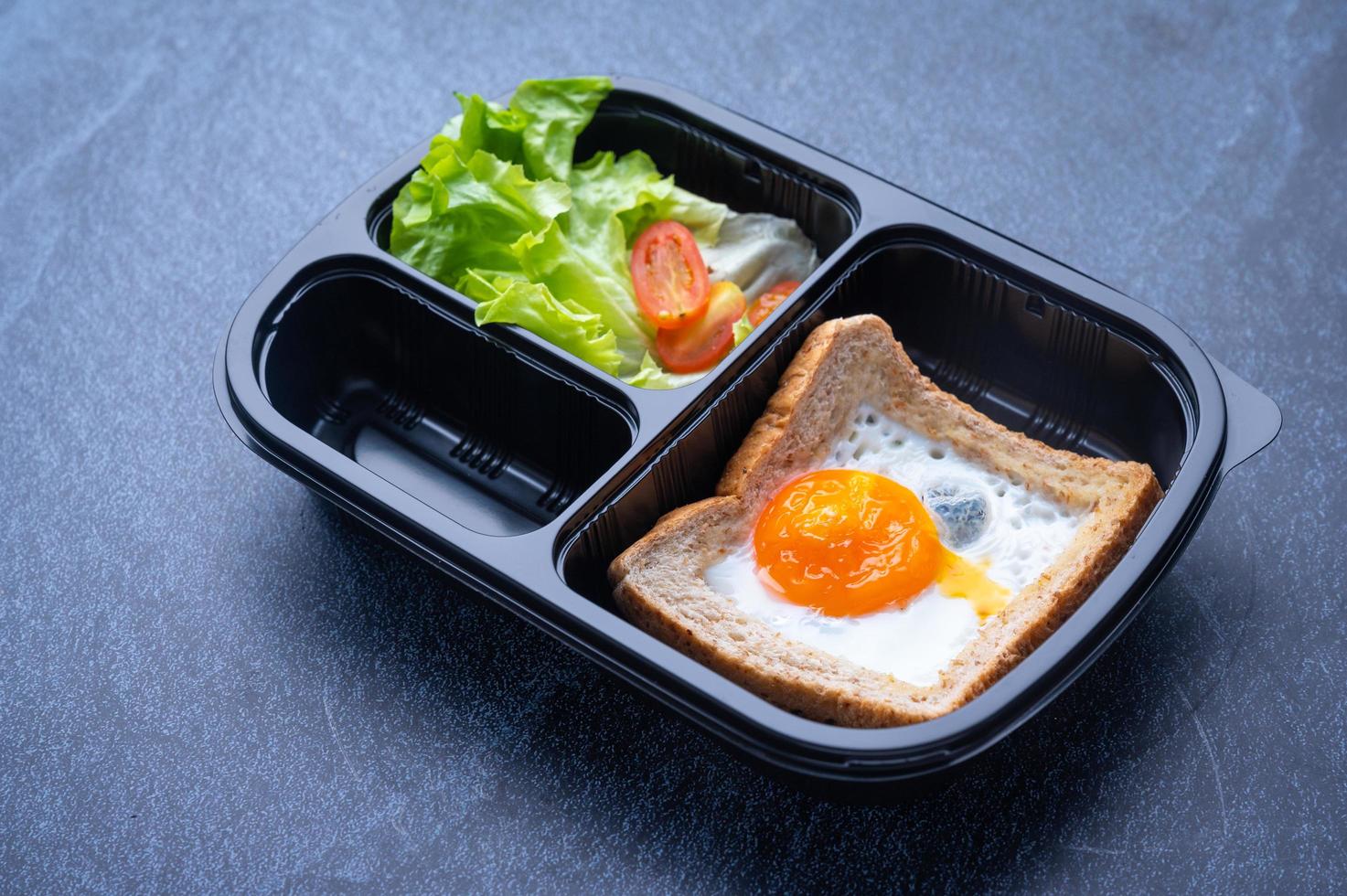 geschnittener Plastiknahrungsmittelbehälter mit Salat, Toast und Spiegelei foto