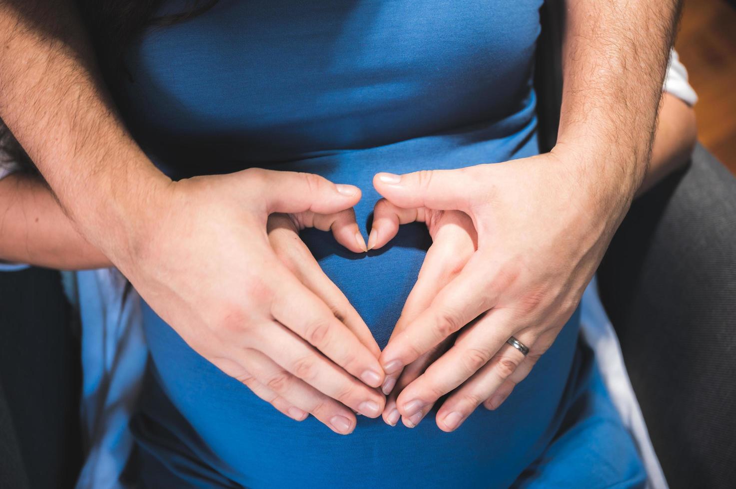 Nahaufnahme der Hände von Mann und Frau zusammen auf dem Bauch der schwangeren Frau foto