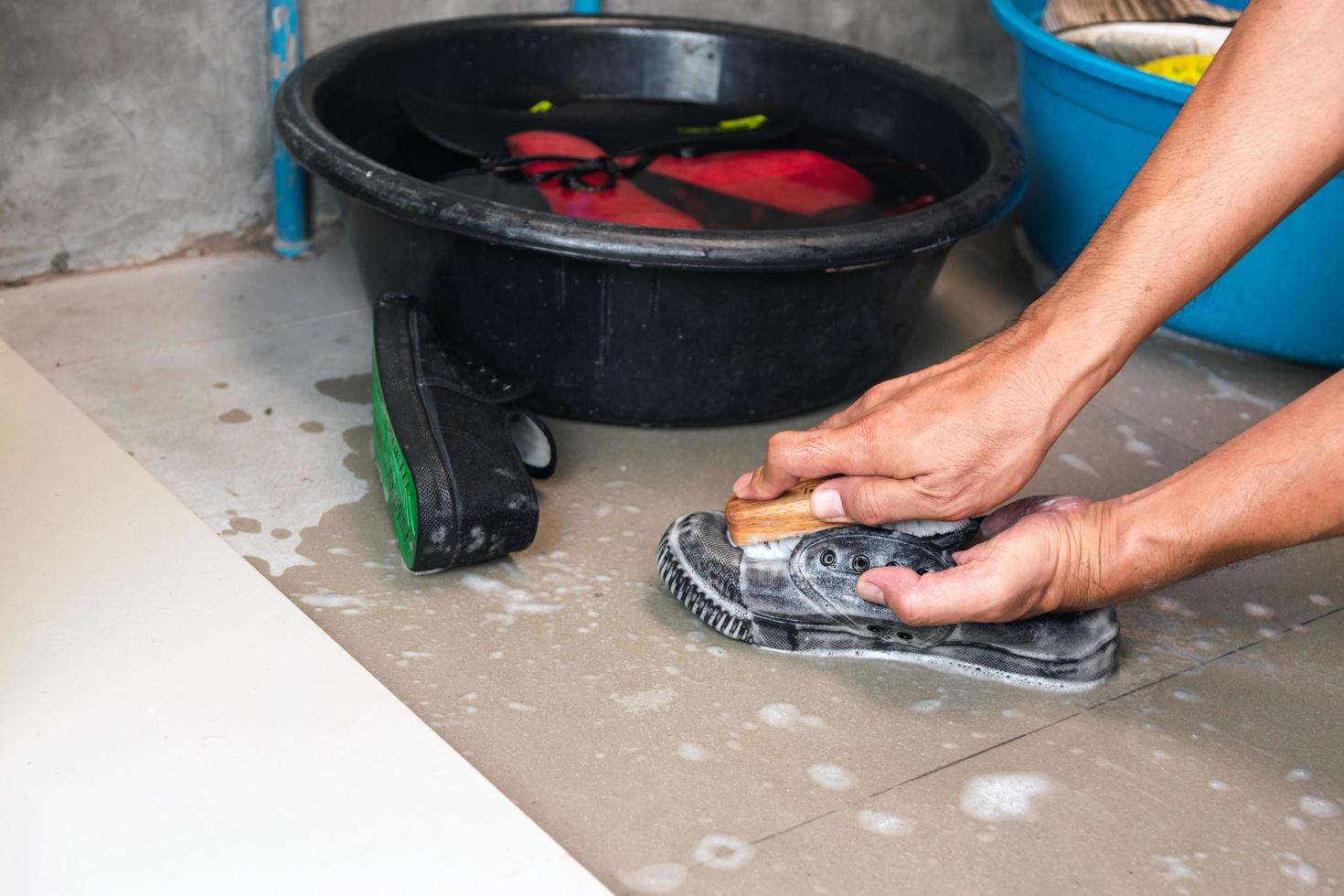 Hände waschen Tennisschuhe neben mit Wasser und Schuhen gefüllten Eimern foto