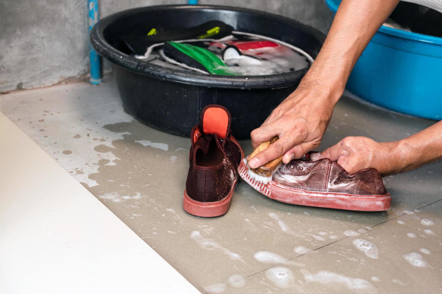 zwei Hände waschen Tennisschuhe neben mit Wasser und Schuhen gefüllten Eimern foto