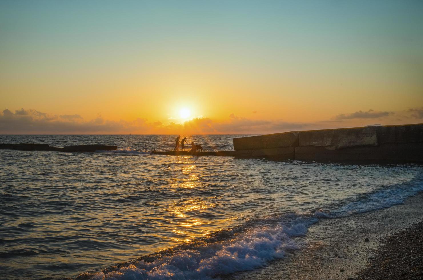 silhouettierte Leute, die am Strand bei Sonnenuntergang in Sotschi, Russland schwimmen foto