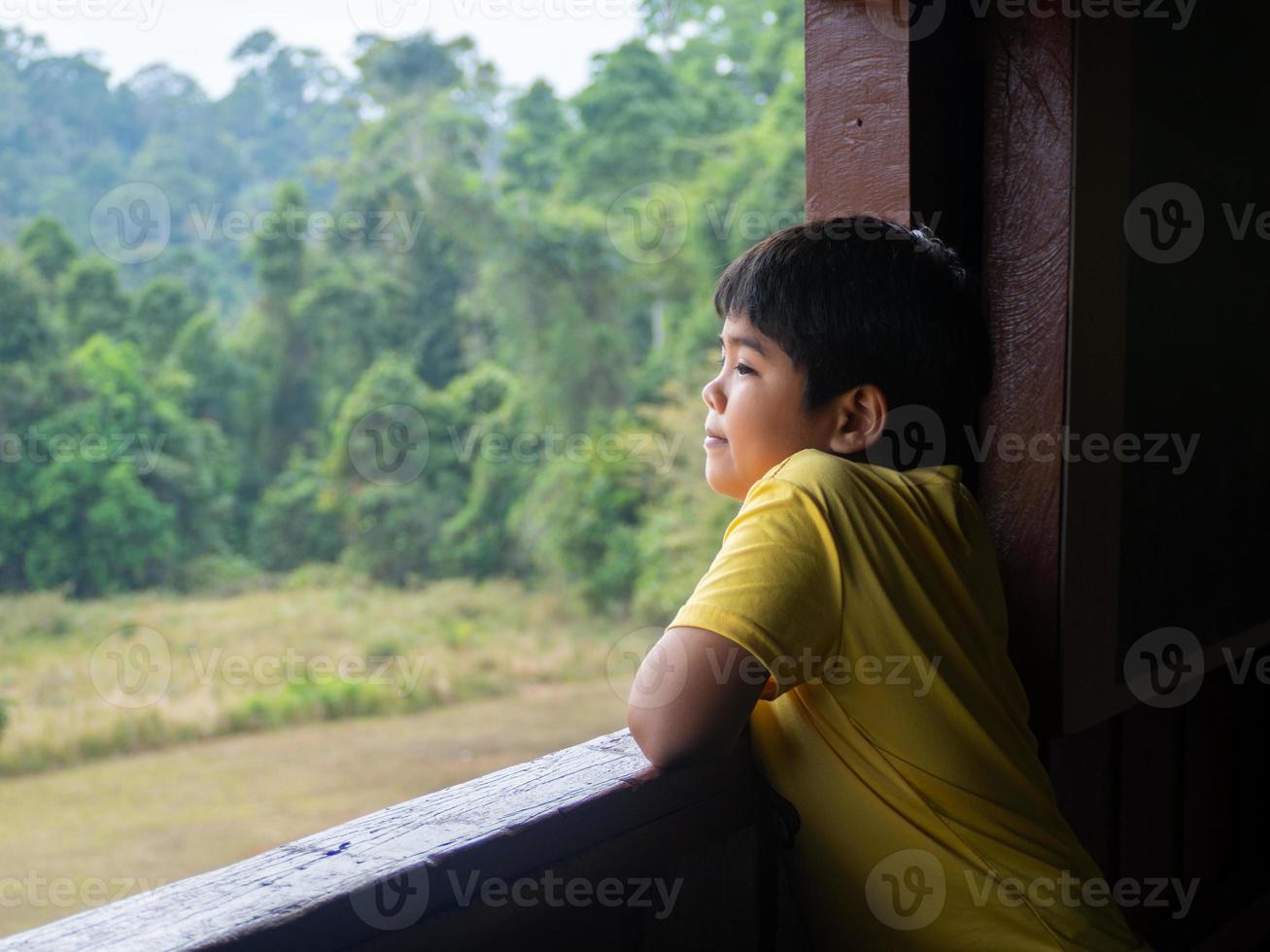 Junge, der aus dem Fenster blickt und den grünen Wald betrachtet foto