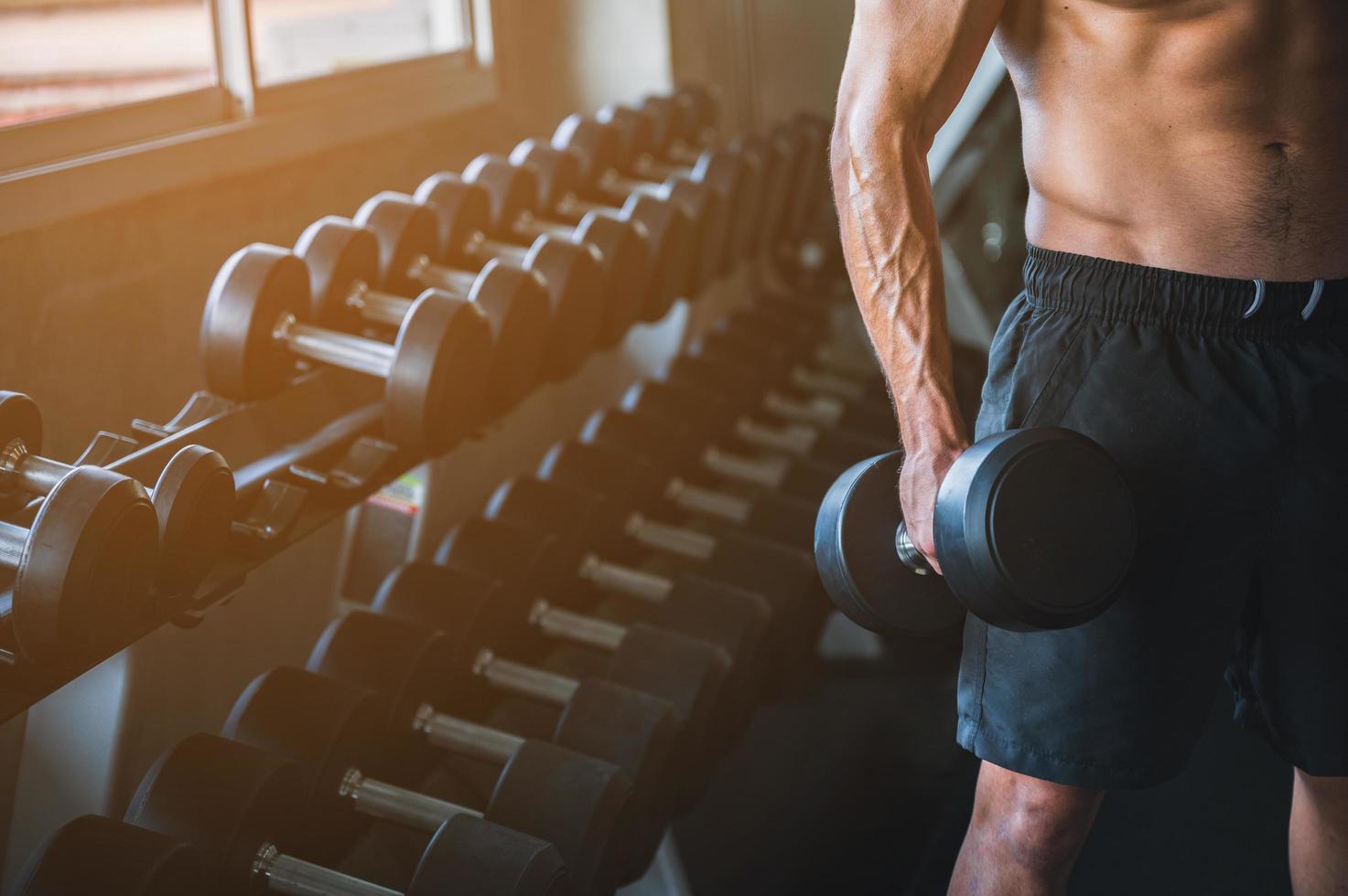 Mann hält eine Hantel in einem Fitnessstudio mit einer Reihe von Hanteln im Hintergrund foto