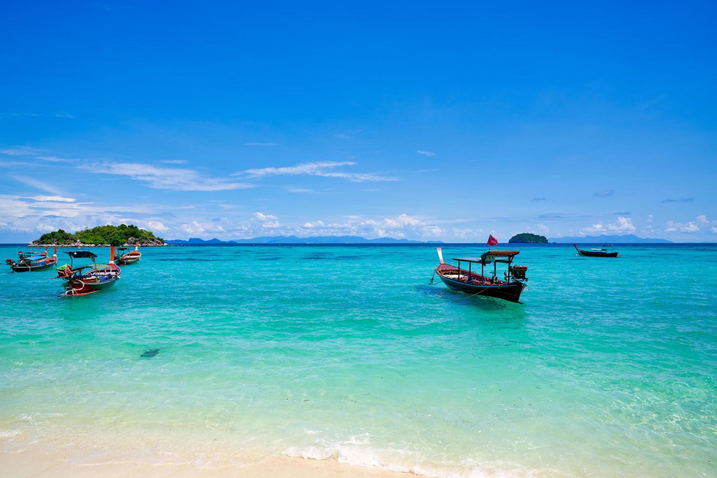 bunte Boote im blauen Wasser mit Strand und bewölktem blauem Himmel auf koh lipe Insel in Thailand foto