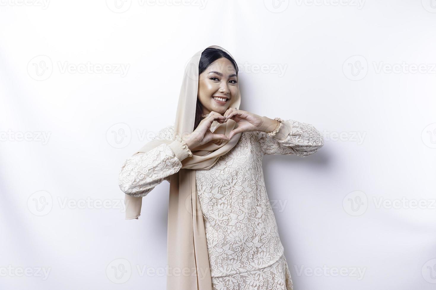 ein glücklich jung asiatisch Frau tragen Hijab fühlt sich romantisch Formen Herz Geste drückt aus zärtlich Gefühle foto