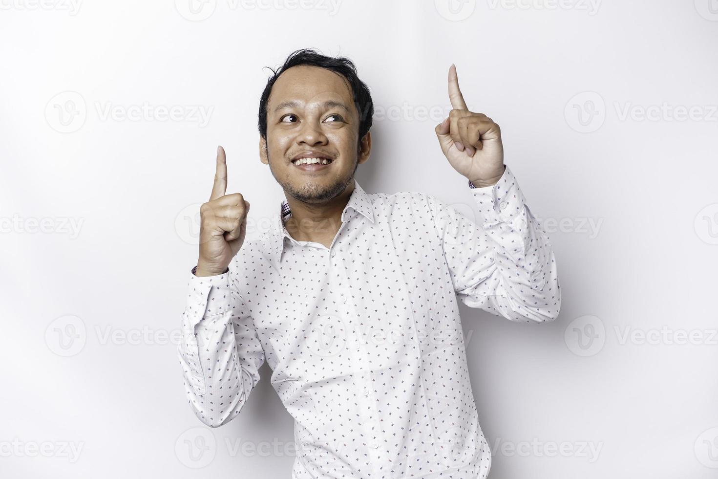 aufgeregt asiatisch Mann tragen Weiß Hemd zeigen beim das Kopieren Raum auf oben von ihn, isoliert durch Weiß Hintergrund foto