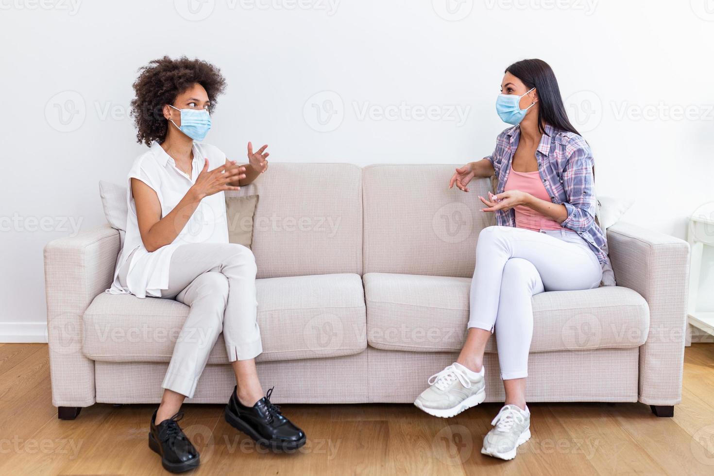 zwei weiblich Beste freunde Sitzung im Sozial Entfernung tragen Gesicht Maske und reden auf das Sofa, verhindern covid 19 Coronavirus Pandemie Infektion Ausbreitung. foto