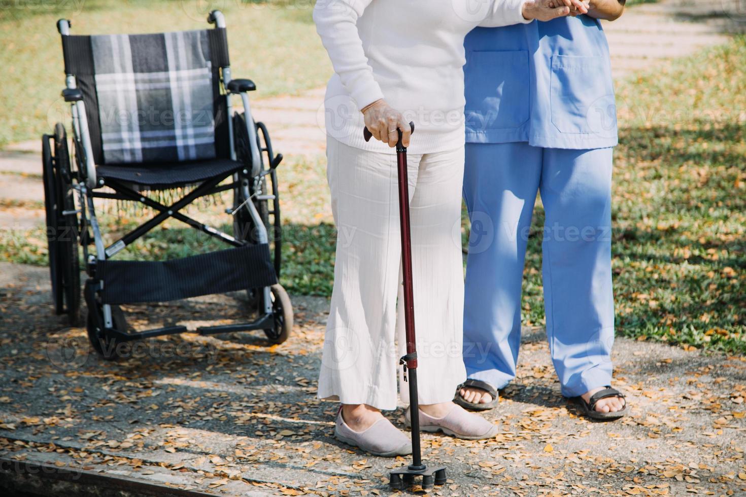 asiatisch jung Pflegekraft Krankenschwester Unterstützung Senior älter männlich Gehen draußen. Spezialist Mädchen Arzt Hilfe und nehmen Pflege von Alten reifen Mann geduldig tun physisch Therapie im Öffentlichkeit Park beim Pflege- heim. foto