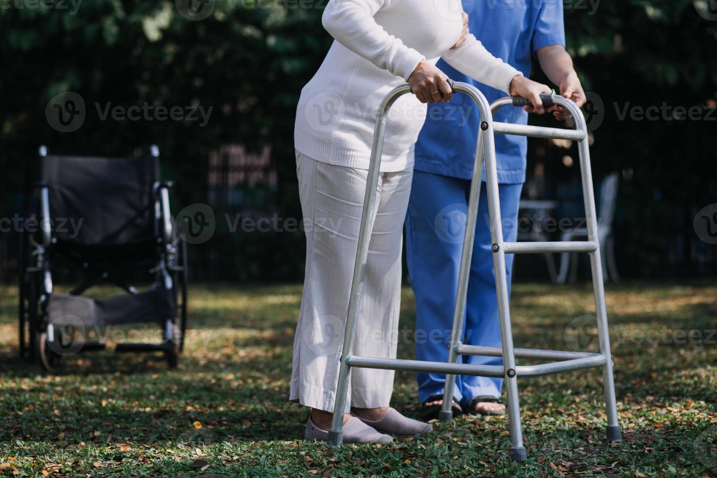 asiatisch jung Pflegekraft Krankenschwester Unterstützung Senior älter männlich Gehen draußen. Spezialist Mädchen Arzt Hilfe und nehmen Pflege von Alten reifen Mann geduldig tun physisch Therapie im Öffentlichkeit Park beim Pflege- heim. foto