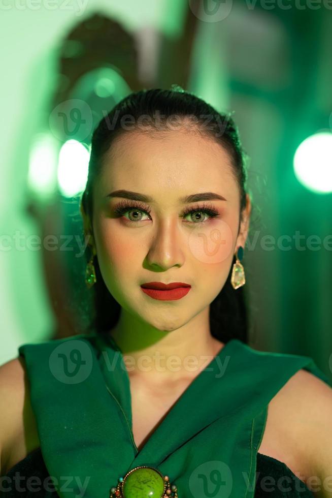 ein schön asiatisch Frau im ein Grün Kleid hat ein sehr exotisch Gesicht mit Ohr und Körper Schmuck während foto