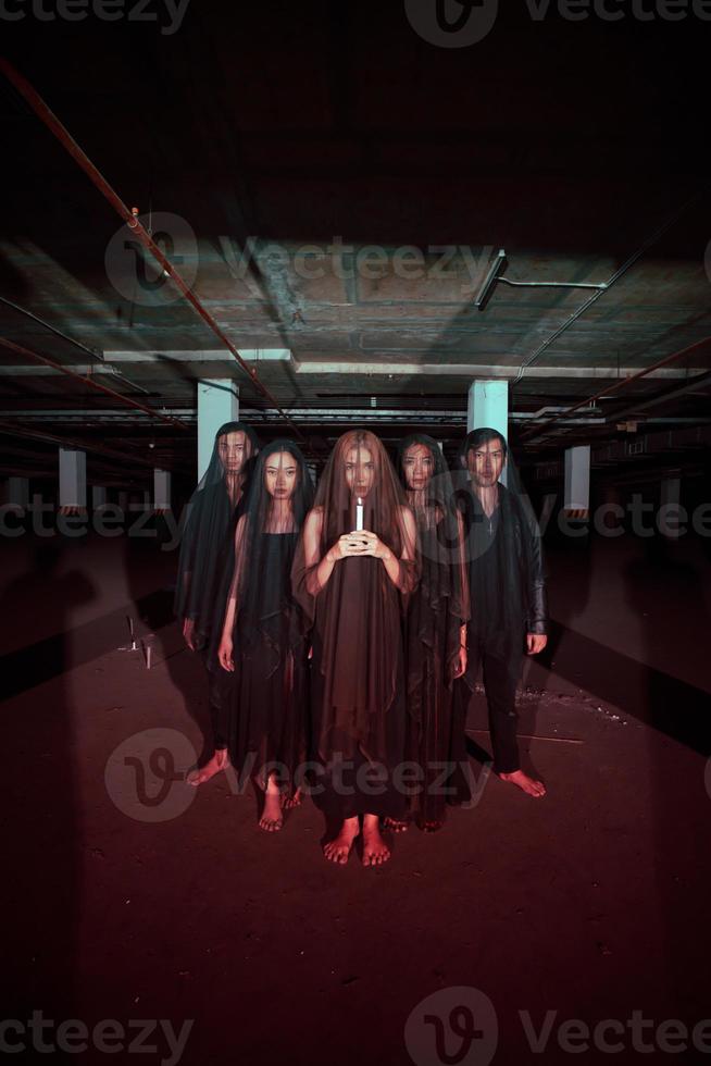 ein Gruppe von Teufel Anbeter im alle schwarz Kleider und transparent Schleier halten Kerzen zusammen während ein Anbetung Ritual im ein Gebäude foto