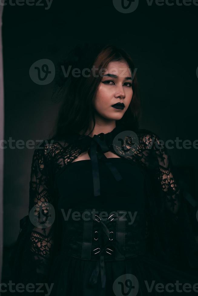 ein unheimlich asiatisch Frau mit schwarz Lippen halten ihr alles schwarz Kleider wann Besuch das Friedhof foto