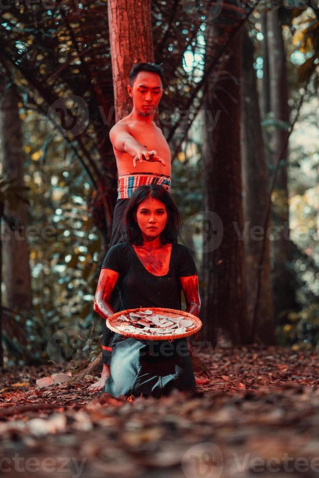 ein asiatisch Frau und Mann wurden Stehen im Vorderseite von ein Baum während Jagd ein Tier im das Mitte von das Wald bis um Sie wurden bedeckt im Blut foto
