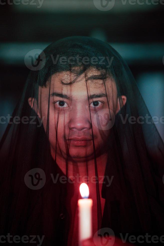 ein asiatisch Mann mit ein transparent Kapuze bedeckt im Blut hält ein Kerze im seine Hand mit ein sehr unheimlich Ausdruck foto