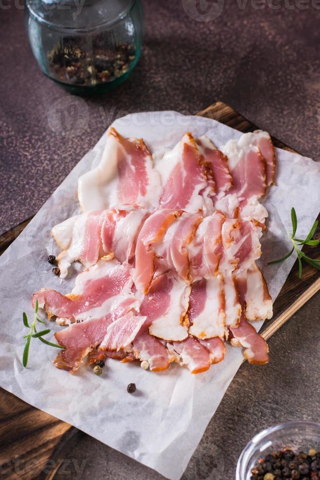 roh Speck Scheiben auf Papier auf ein Schneiden Tafel auf das Tisch. herzhaft Snack. Vertikale Aussicht foto