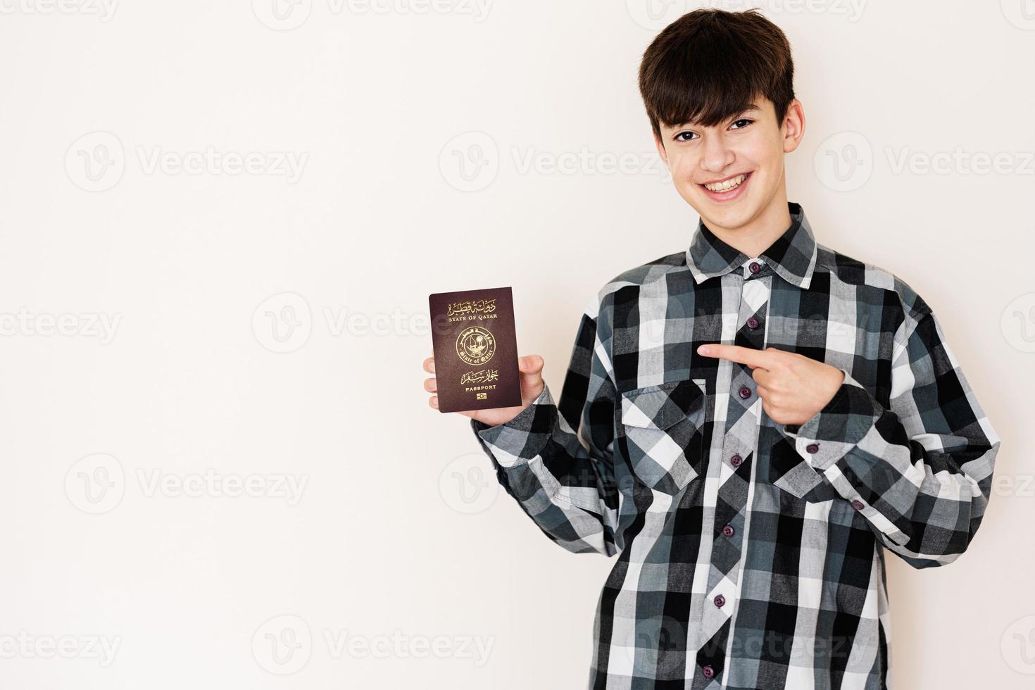 jung Teenager Junge halten Katar Reisepass suchen positiv und glücklich Stehen und lächelnd mit ein zuversichtlich Lächeln gegen Weiß Hintergrund. foto