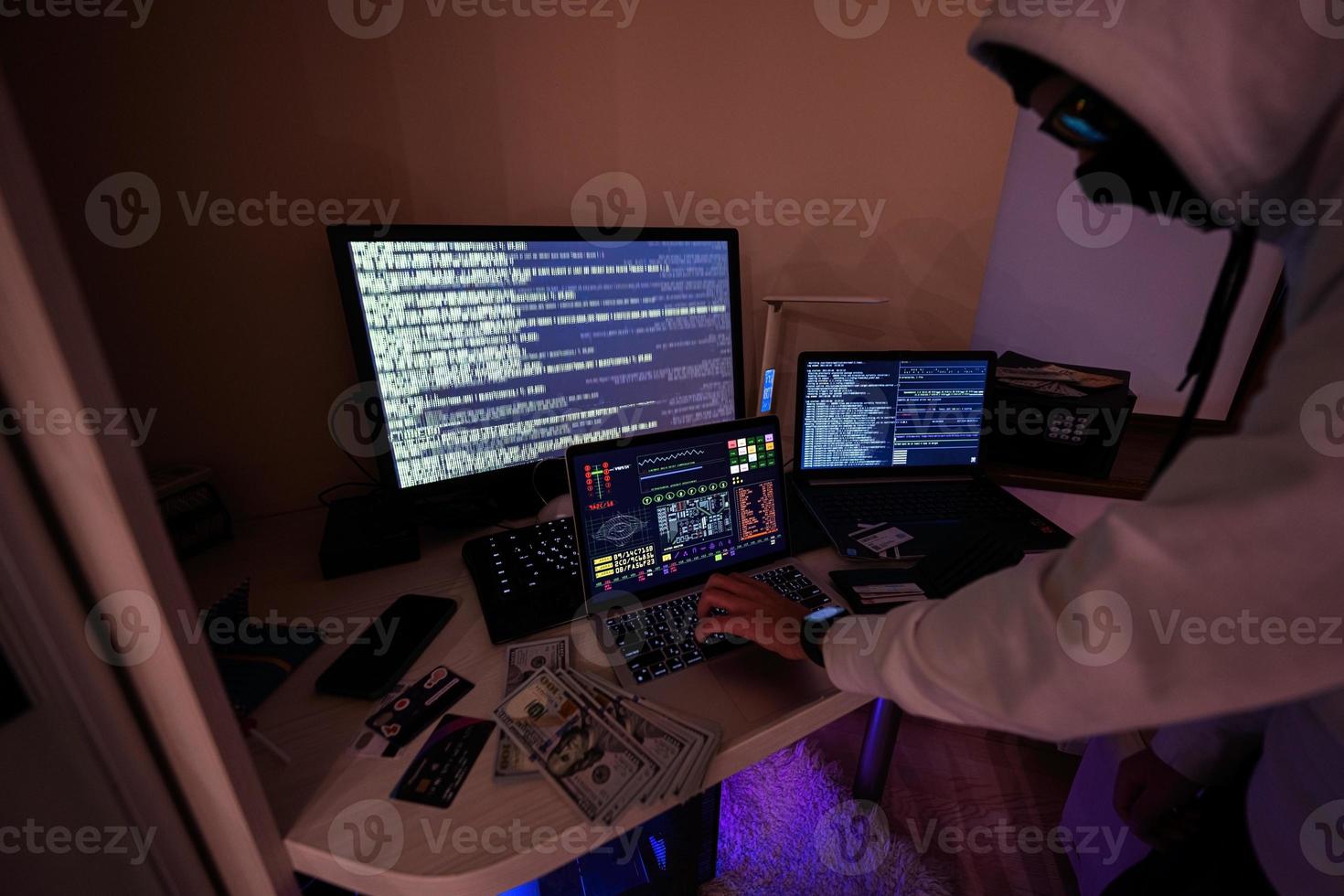 Junge Hacker betrügerisch verwenden Anerkennung Karte zum Zahlung. Internet Diebstahl . Mann tragen ein Sturmhaube und halten ein Anerkennung Karte während hinter ein Laptop. foto