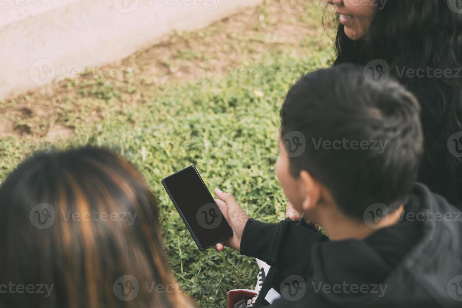 Aussicht desde Atren grupo de Latinos riendo gesendet en el suelo en un Parque con un Smartphone foto