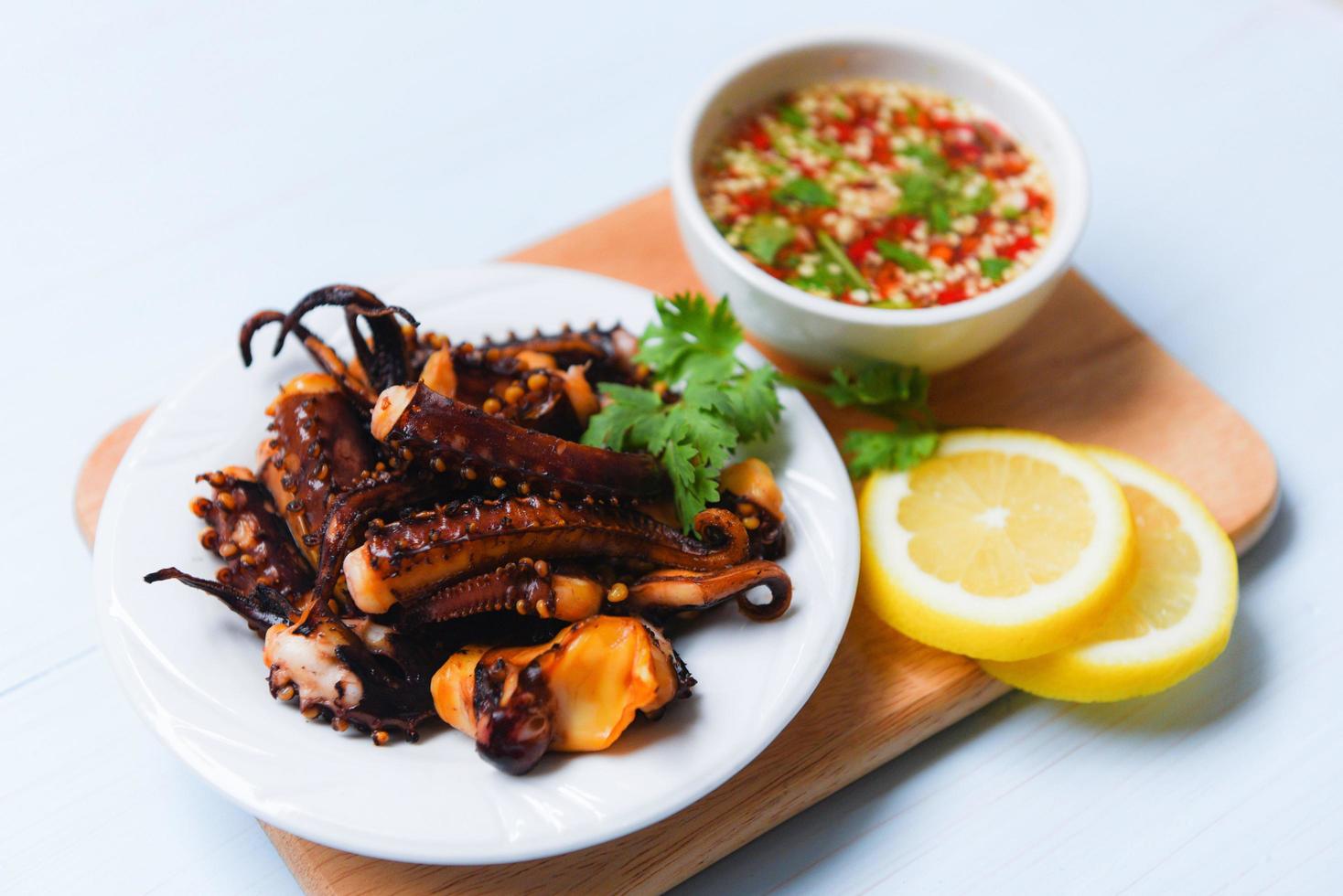 Tintenfisch Salat mit Zitrone Kräuter und Gewürze auf Weiß Teller - - Tentakeln Tintenfisch gegrillt Vorspeise Essen heiß und würzig Chili Soße Meeresfrüchte gekocht serviert auf hölzern Schneiden Tafel im das Restaurant foto