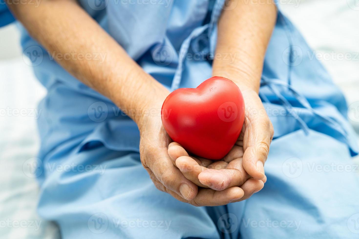 asiatisch Alten Frau geduldig halten rot Herz im ihr Hand auf Bett im Krankenhaus, gesund stark medizinisch Konzept. foto